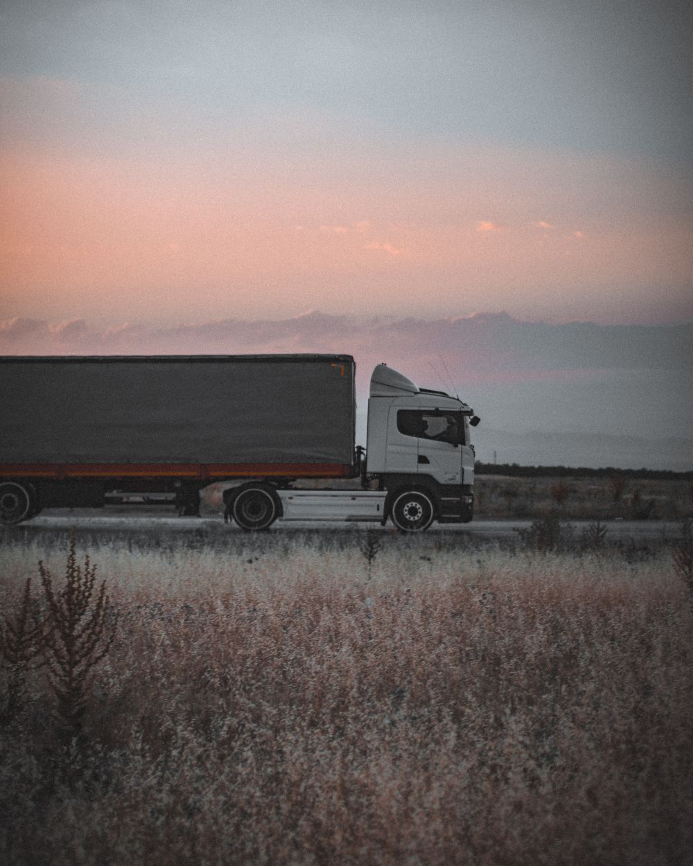A freight truck travelling along a road at sunset